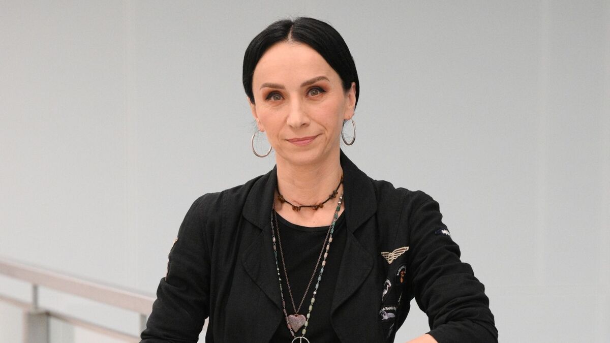 Renata Przemyk stoi w studiu programu „Pytanie na śniadanie” i patrzy w stronę aparatu. Ma ciemne włosy zaczesane do tyłu, kolczyki w kształcie kół oraz czarną marynarkę z naszyjnikiem z drobnych koralików i zawieszką w kształcie serca. Tło jest jasne i neutralne.