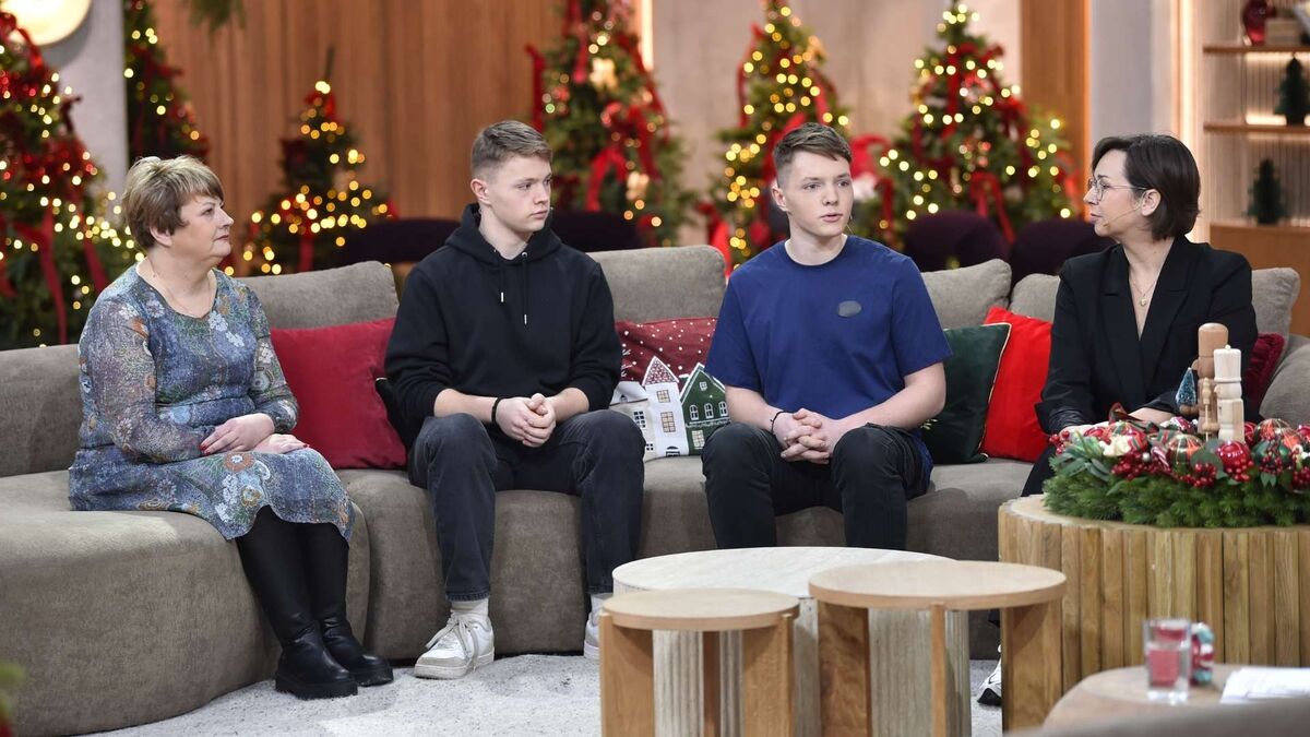 Cztery osoby siedzą na beżowej kanapie w świątecznie udekorowanym studio i prowadzą rozmowę. Po lewej widać starszą kobietę w wzorzystej sukience, obok niej siedzi nastolatek w czarnej bluzie z kapturem, a dalej młody mężczyzna w niebieskiej koszulce, zwrócony w stronę prowadzącej. Po prawej stronie znajduje się kobieta w czarnym stroju z mikrofonem przy policzku, a w tle migoczą choinki z lampkami i czerwonymi ozdobami.